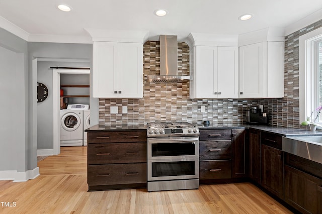 kitchen featuring double oven range, washing machine and clothes dryer, dark brown cabinets, and wall chimney range hood