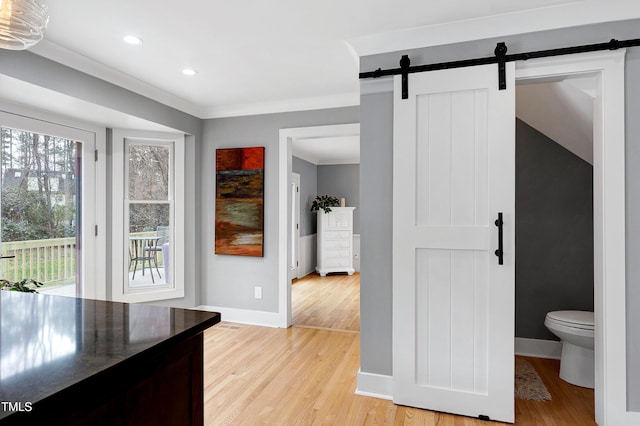 interior space with a barn door, light wood-style floors, baseboards, and ornamental molding