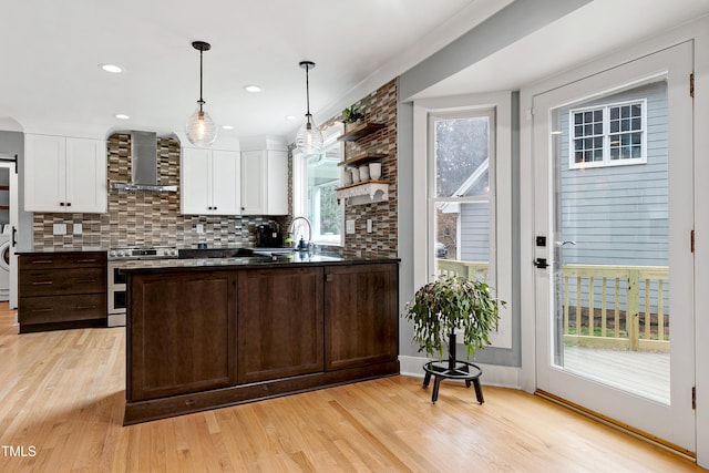 kitchen with wall chimney range hood, dark countertops, stainless steel range with electric stovetop, and white cabinets