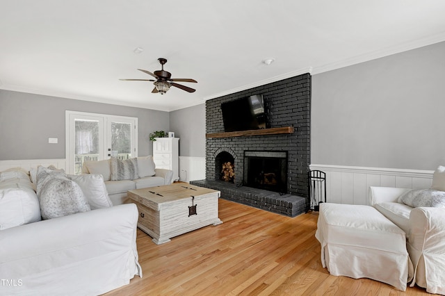 living area featuring wainscoting, a fireplace, crown molding, and ceiling fan