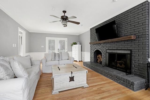 living room with light wood finished floors, a fireplace, crown molding, wainscoting, and ceiling fan