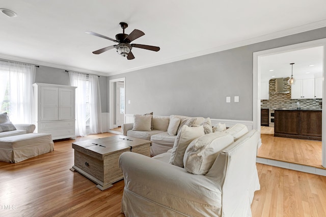 living room featuring light wood-type flooring, ceiling fan, and ornamental molding