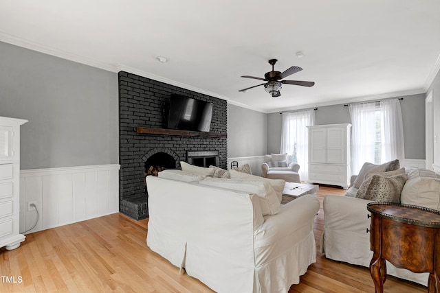 living room with light wood-type flooring, ceiling fan, a fireplace, and ornamental molding