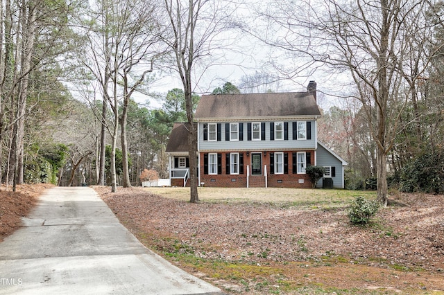 colonial house with brick siding, driveway, and a chimney