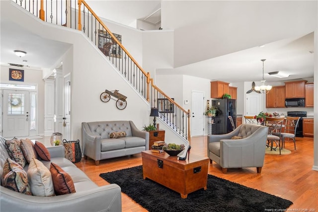 living room with light wood finished floors, a high ceiling, stairway, and an inviting chandelier