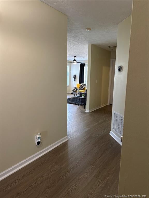 hallway featuring visible vents, a textured ceiling, baseboards, and dark wood-style flooring