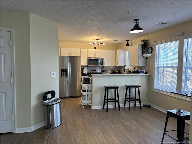 kitchen featuring a kitchen bar, backsplash, wood finished floors, a peninsula, and appliances with stainless steel finishes