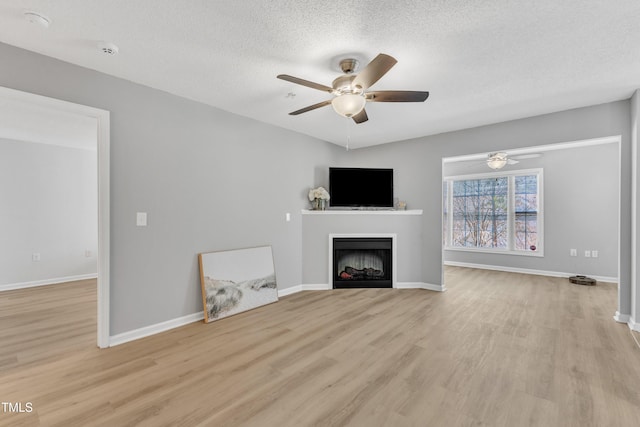 unfurnished living room with baseboards, light wood-type flooring, a fireplace, a textured ceiling, and a ceiling fan