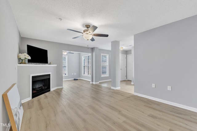 unfurnished living room featuring light wood-type flooring, a ceiling fan, a textured ceiling, a fireplace, and baseboards