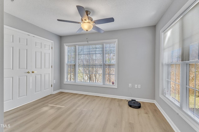 unfurnished bedroom with a closet, light wood-style flooring, a textured ceiling, and baseboards