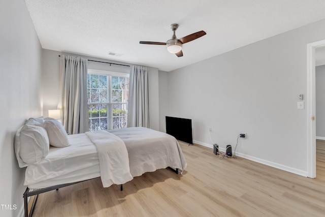 bedroom with visible vents, a ceiling fan, a textured ceiling, light wood-style floors, and baseboards