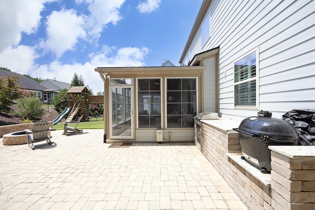 view of patio with area for grilling, a playground, a sunroom, and an outdoor fire pit