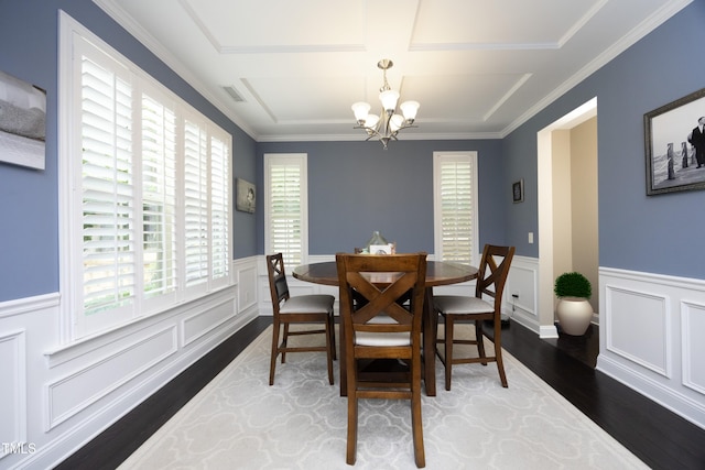 dining space featuring visible vents, a notable chandelier, ornamental molding, wood finished floors, and wainscoting