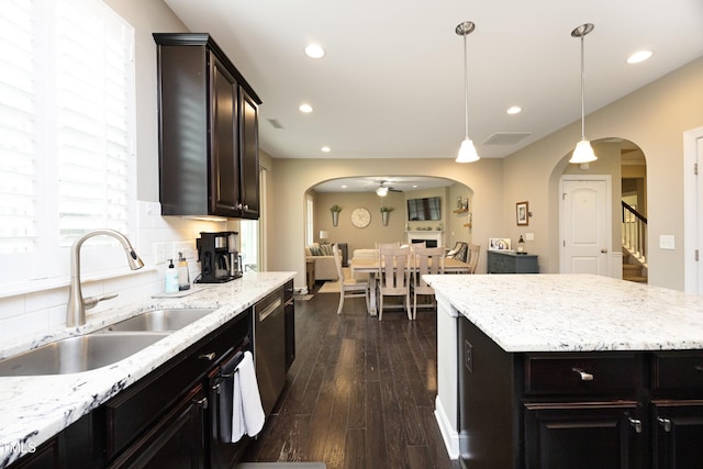 kitchen with tasteful backsplash, dishwasher, dark wood-style floors, arched walkways, and a sink