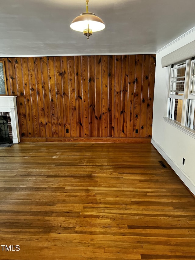 unfurnished living room featuring visible vents, heating unit, wood finished floors, wooden walls, and a brick fireplace