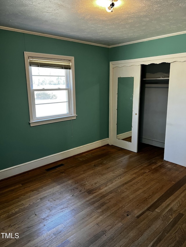 unfurnished bedroom with visible vents, ornamental molding, a textured ceiling, dark wood finished floors, and a closet