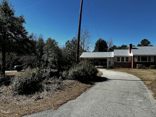 view of front of house featuring aphalt driveway, an attached carport, a chimney, and metal roof