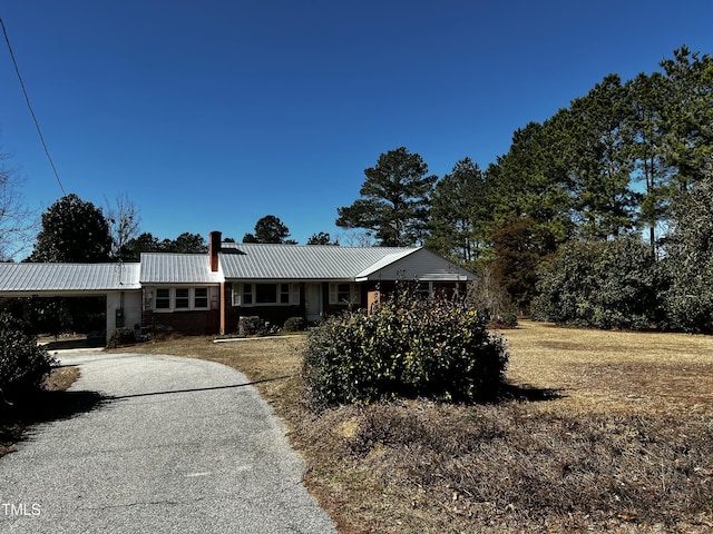 ranch-style home with metal roof, a carport, a chimney, and aphalt driveway