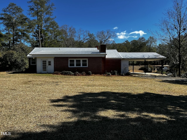 view of front of house featuring an attached carport, a front lawn, a chimney, and metal roof