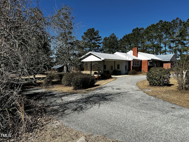 ranch-style home with aphalt driveway, metal roof, and a chimney