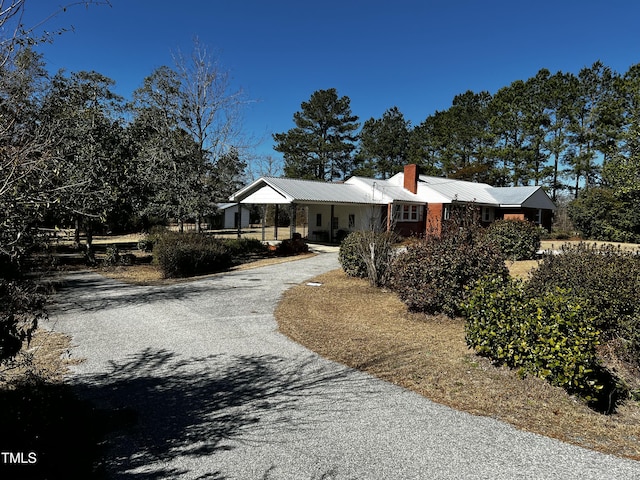 ranch-style house featuring a chimney, driveway, and metal roof