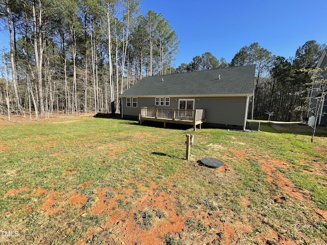 back of house with a shingled roof, a deck, and a lawn