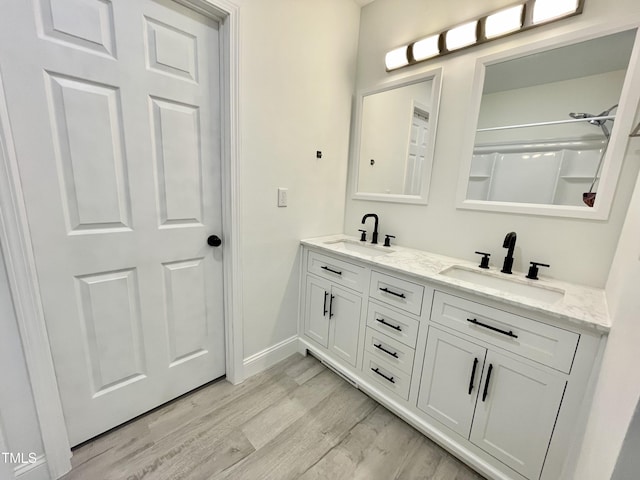 full bath with a sink, a shower, double vanity, and wood finished floors