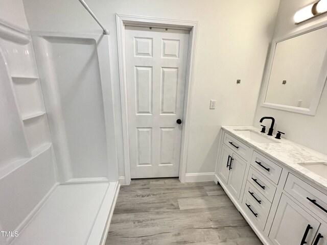 full bath featuring baseboards, double vanity, a shower, a sink, and wood finished floors