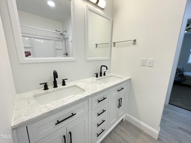 ensuite bathroom featuring wood finished floors, double vanity, a sink, and baseboards