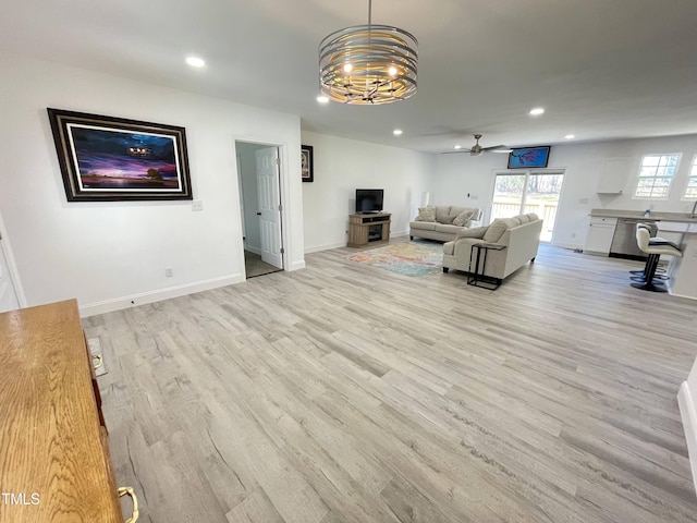 unfurnished living room featuring recessed lighting, light wood-style flooring, baseboards, and ceiling fan with notable chandelier