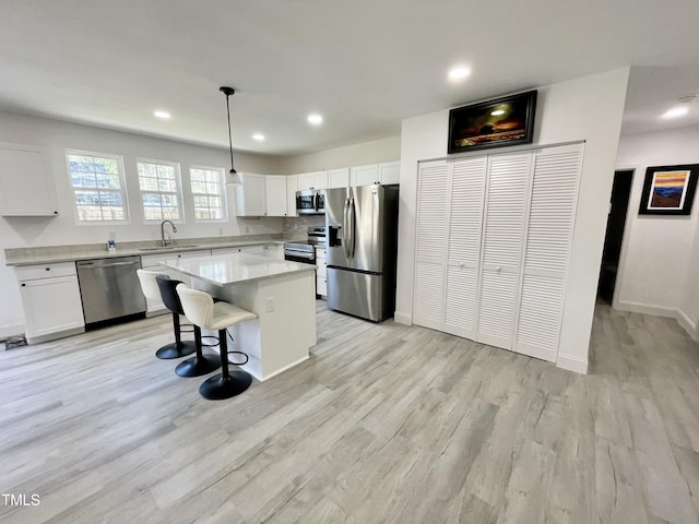 kitchen with light wood-type flooring, white cabinets, a kitchen island, a sink, and stainless steel appliances