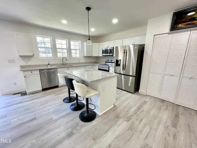 kitchen featuring a center island, a sink, light wood finished floors, white cabinetry, and stainless steel appliances