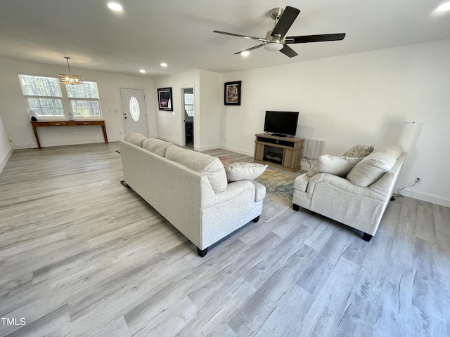 living room with recessed lighting, light wood-style flooring, ceiling fan with notable chandelier, and baseboards