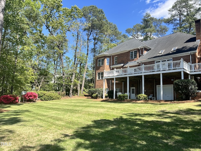 rear view of property featuring a lawn, brick siding, a deck, and a garage