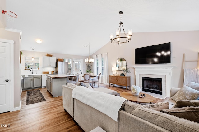 living area with a fireplace with flush hearth, lofted ceiling, an inviting chandelier, and light wood finished floors