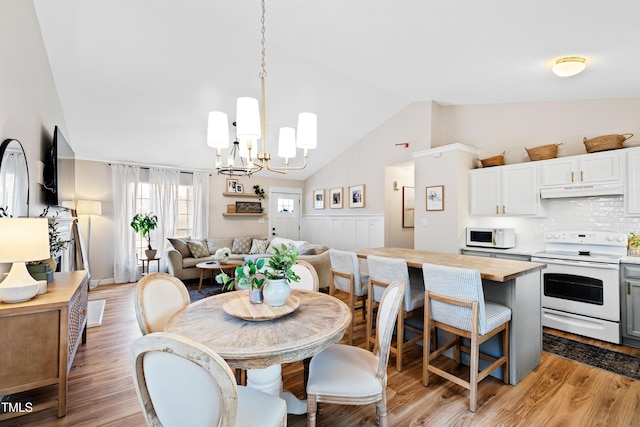 dining area with a notable chandelier, light wood-style floors, and vaulted ceiling