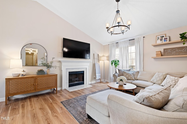 living room featuring a premium fireplace, baseboards, an inviting chandelier, and light wood-style flooring