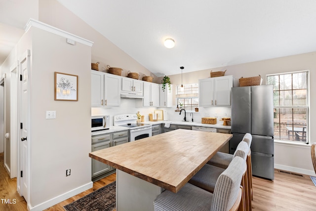 kitchen featuring light wood-type flooring, a kitchen bar, white appliances, and lofted ceiling