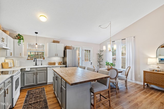 kitchen with gray cabinetry, under cabinet range hood, white appliances, a breakfast bar area, and wooden counters