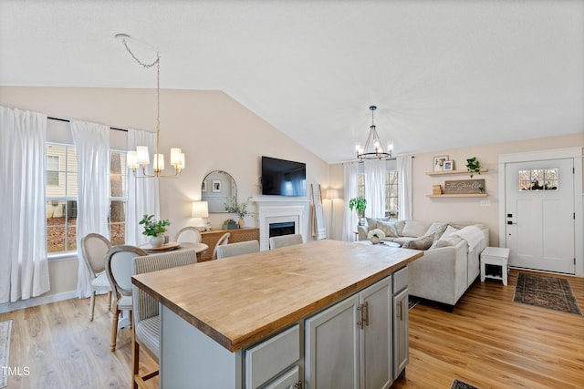 kitchen featuring a notable chandelier, gray cabinetry, a fireplace, wooden counters, and vaulted ceiling