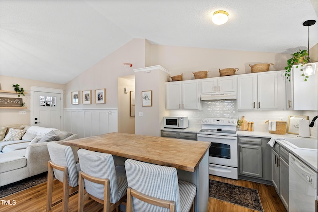 kitchen featuring gray cabinetry, under cabinet range hood, open floor plan, dark wood finished floors, and white appliances