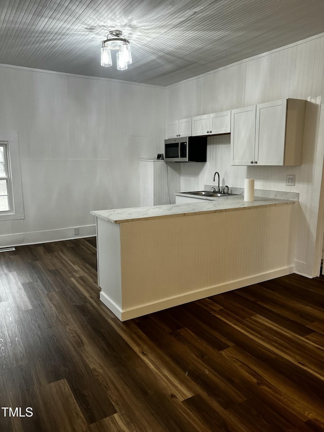 kitchen with light stone countertops, a peninsula, a sink, dark wood-type flooring, and stainless steel microwave