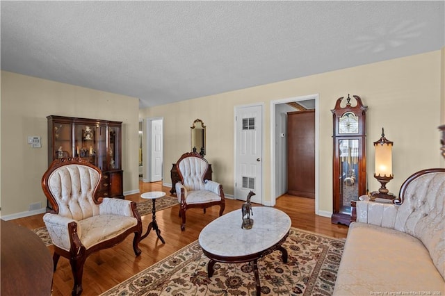 living area with visible vents, baseboards, a textured ceiling, and wood finished floors