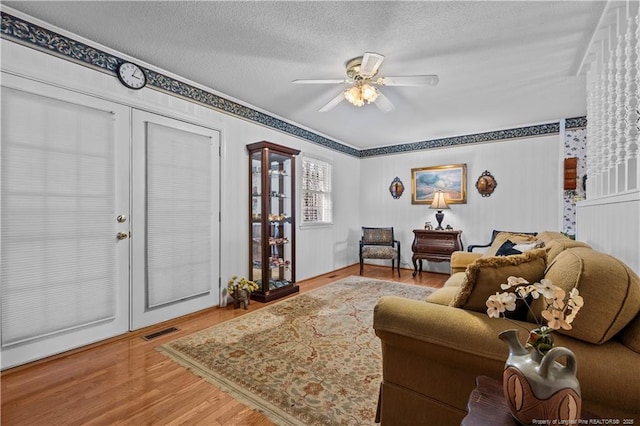 living area with a ceiling fan, wood finished floors, visible vents, and a textured ceiling