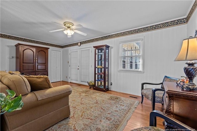 living area featuring visible vents, ornamental molding, a ceiling fan, and light wood finished floors