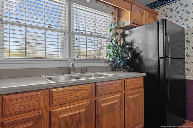 kitchen with a wealth of natural light, brown cabinets, freestanding refrigerator, and a sink