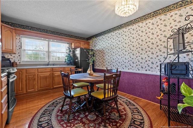 dining space featuring light wood-style floors, a textured ceiling, an inviting chandelier, and wallpapered walls