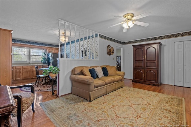 living area featuring ceiling fan with notable chandelier, wood finished floors, wallpapered walls, and a textured ceiling