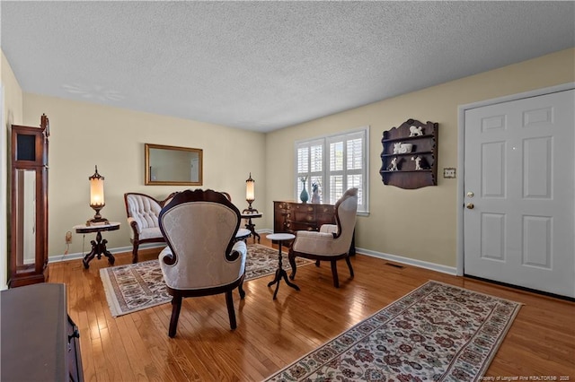 living area featuring hardwood / wood-style floors, baseboards, and a textured ceiling