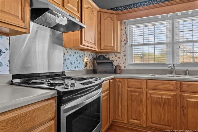 kitchen with stainless steel electric range oven, wallpapered walls, a sink, under cabinet range hood, and a wealth of natural light